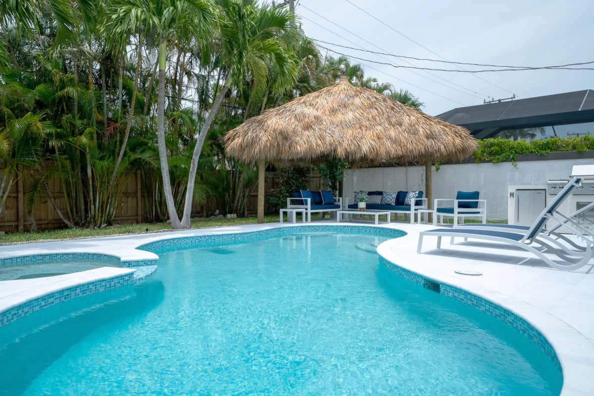 View of a triangular tiki from across a pool in a backyard.
