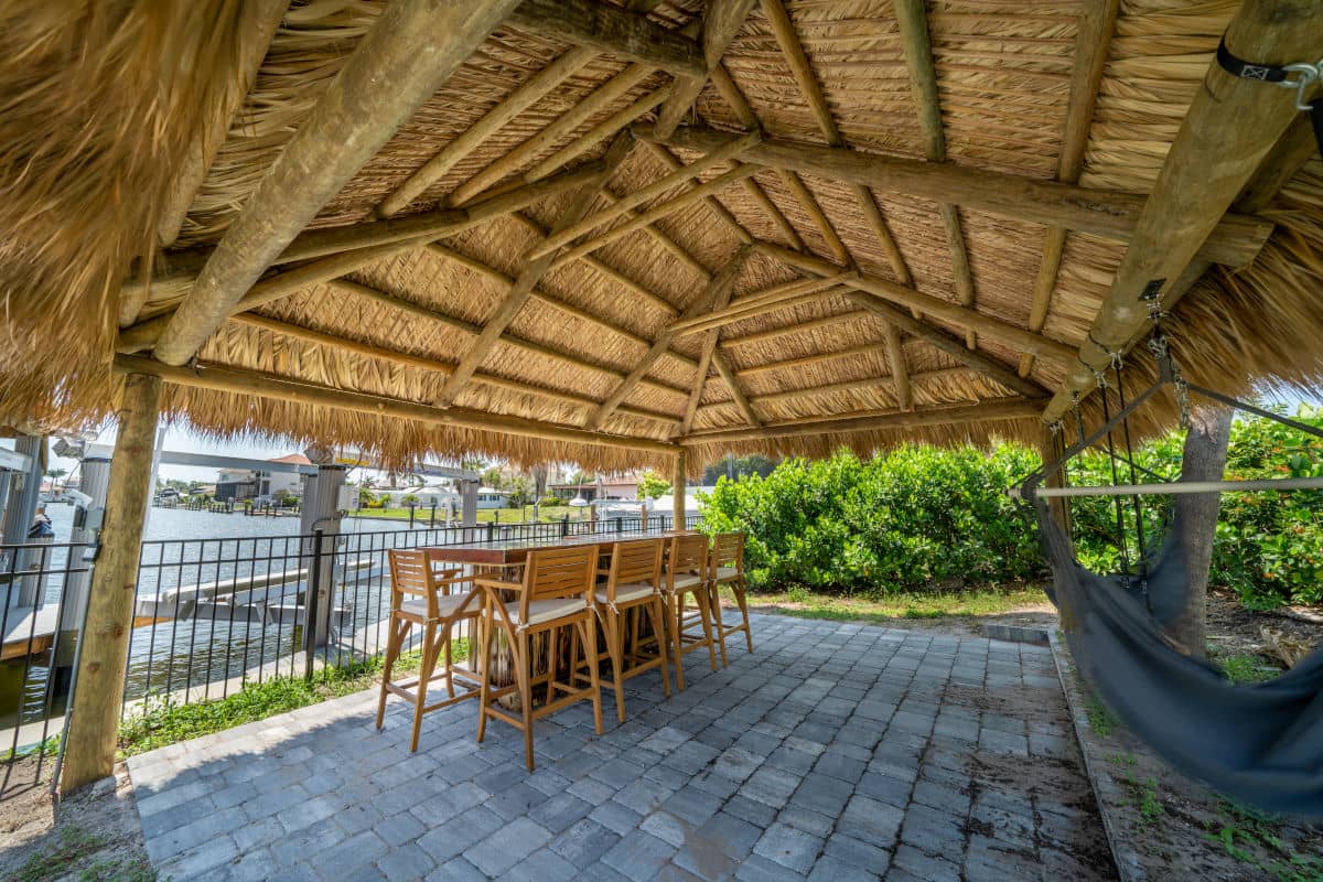 Waterside tiki with table and chairs and a hammock built over a pavered area.