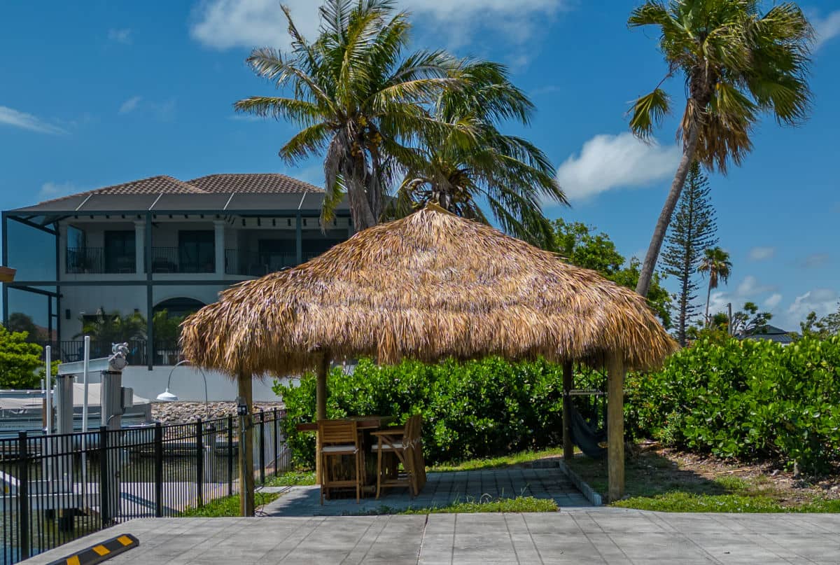 Tiki built next to a canal with bushes surrounding two sides and a paver floor.