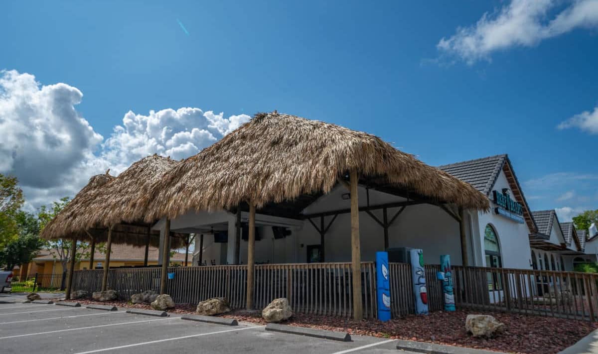 Commercial tiki seating area between a parking lot and a restaurant building.