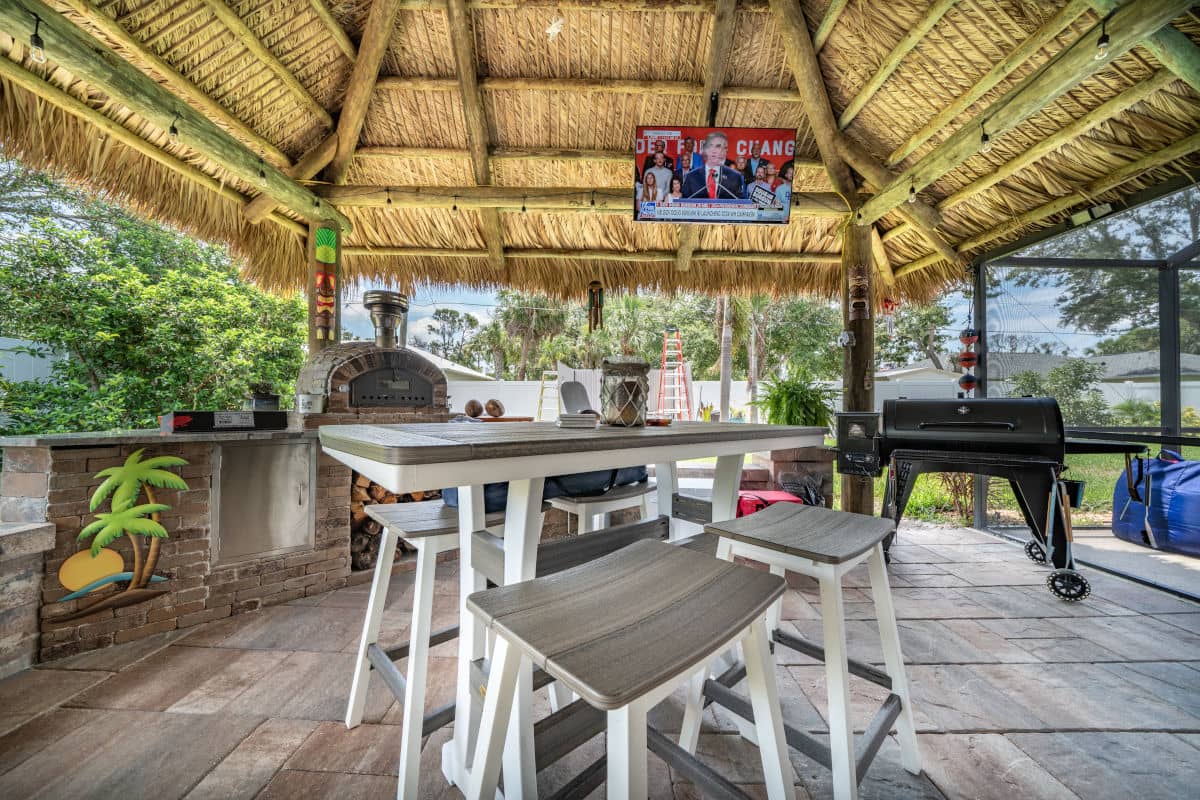 Back yard tiki built over an outdoor kitchen area with a grill next to a seating area.